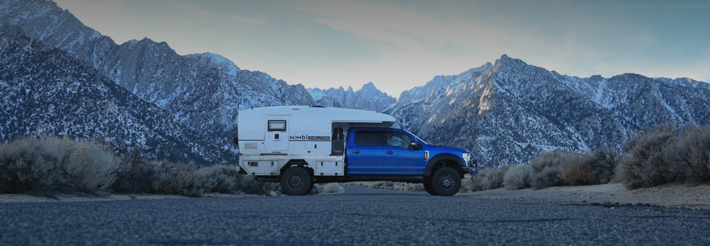 Blue truck with camper attached by some mountains